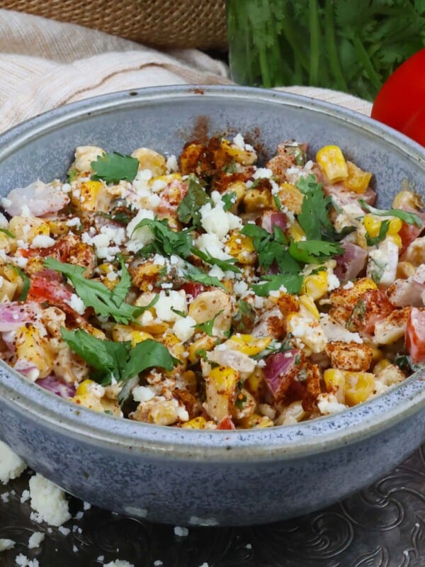 a blue bowl filled with Mexican street corn salad next to a red bell pepper and cilantro