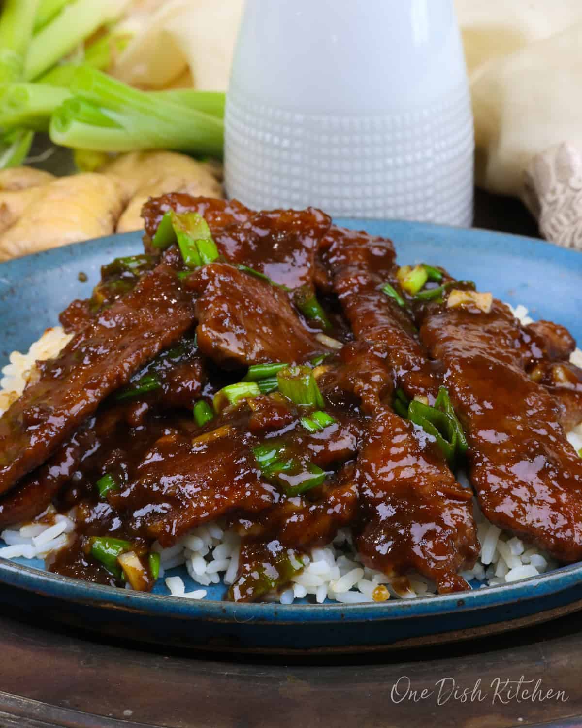a single serving of mongolian beef over white rice on a blue plate.