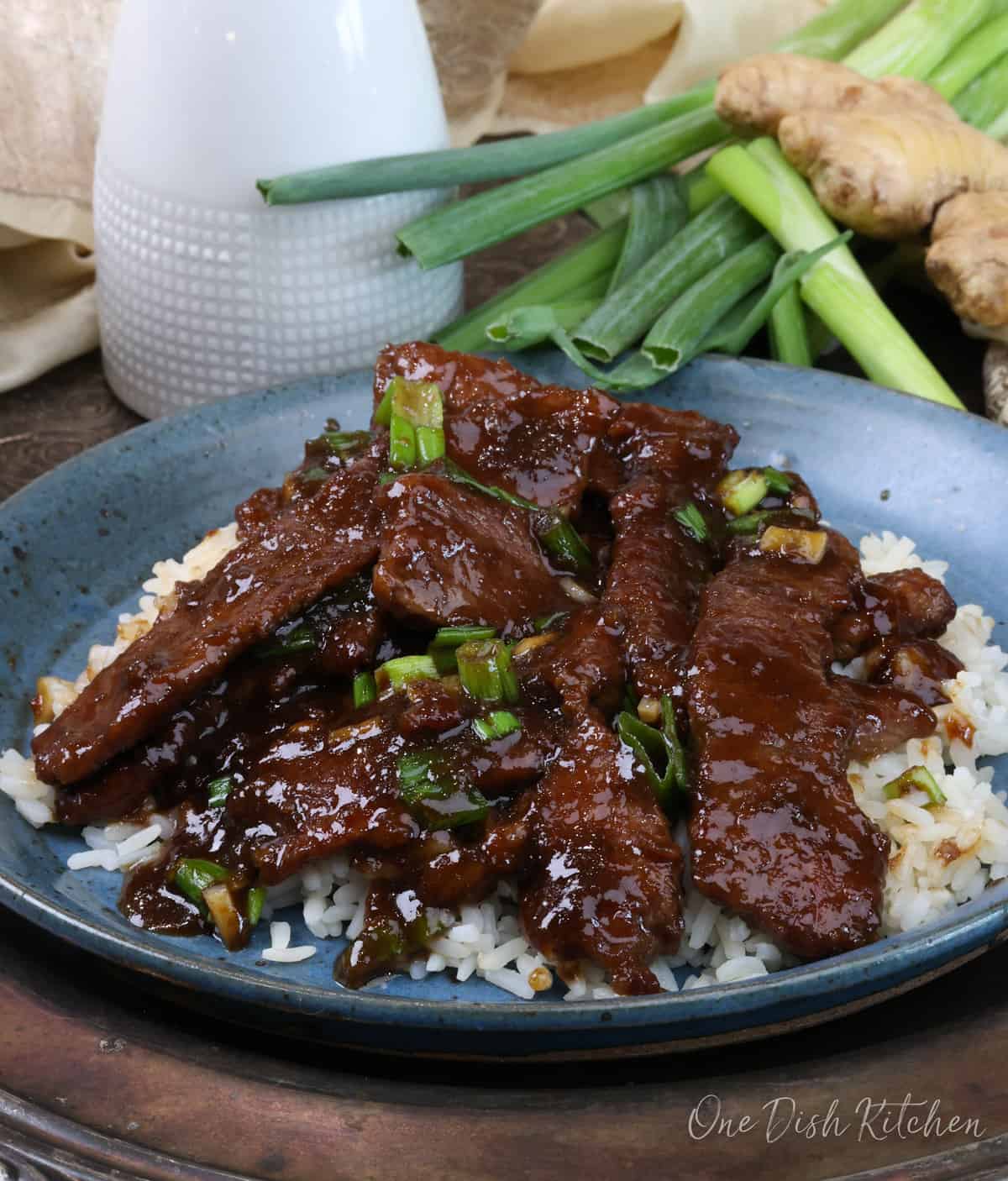 a plate of white rice topped with mongolian beef and its sauce next to a white bottle of soy sauce.