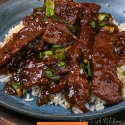 mongolian beef over white rice on a blue plate.