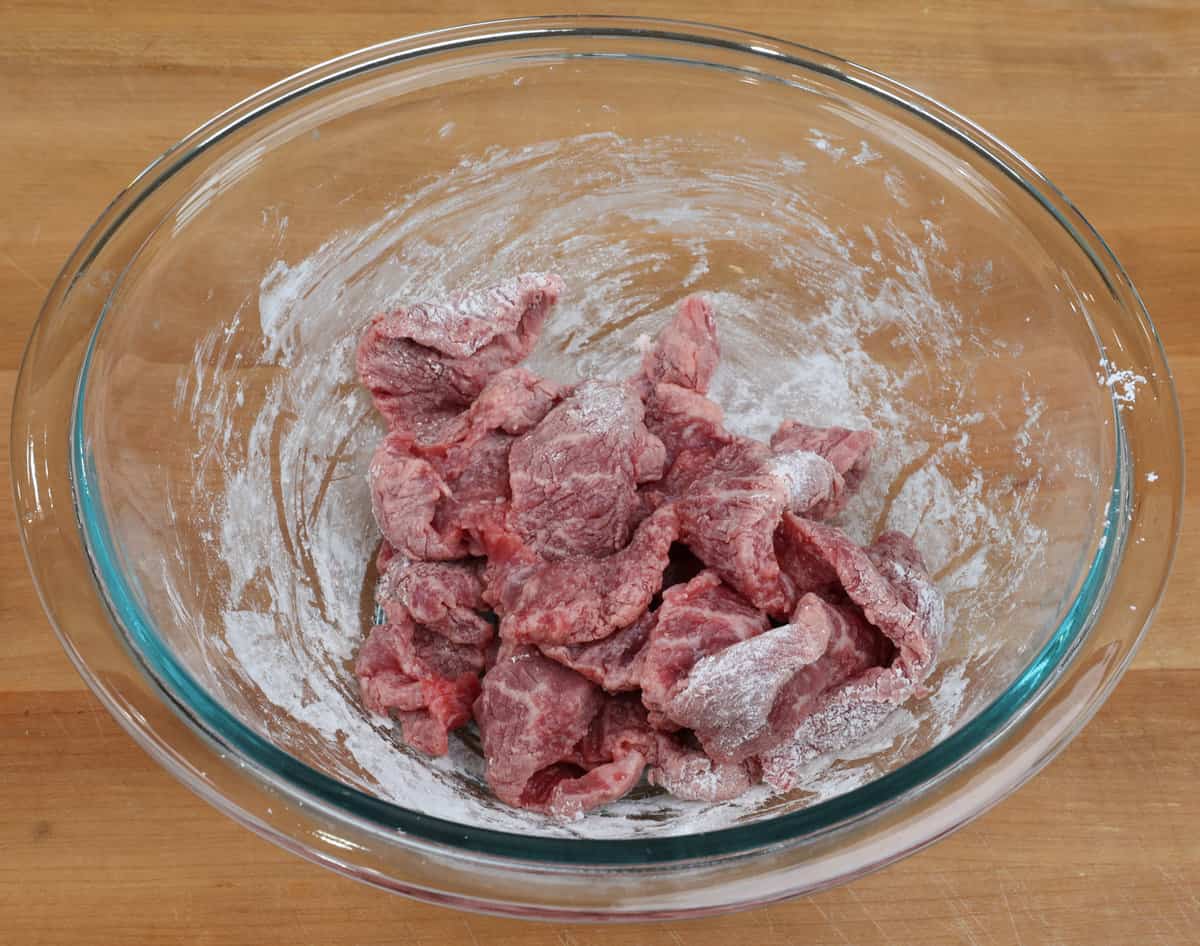 slices of steak in a bowl tossed with cornstarch.
