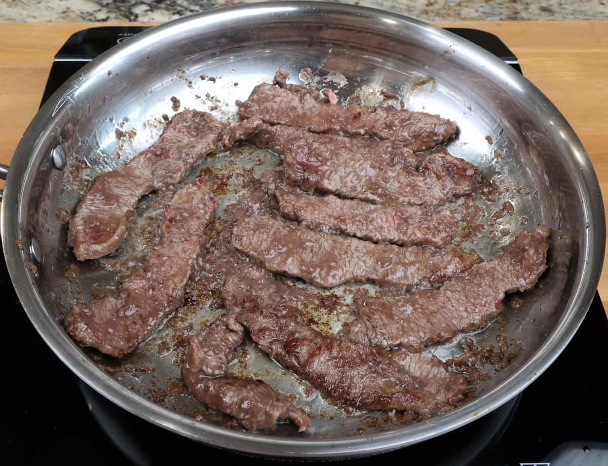 strips of steak cooking in a skillet.