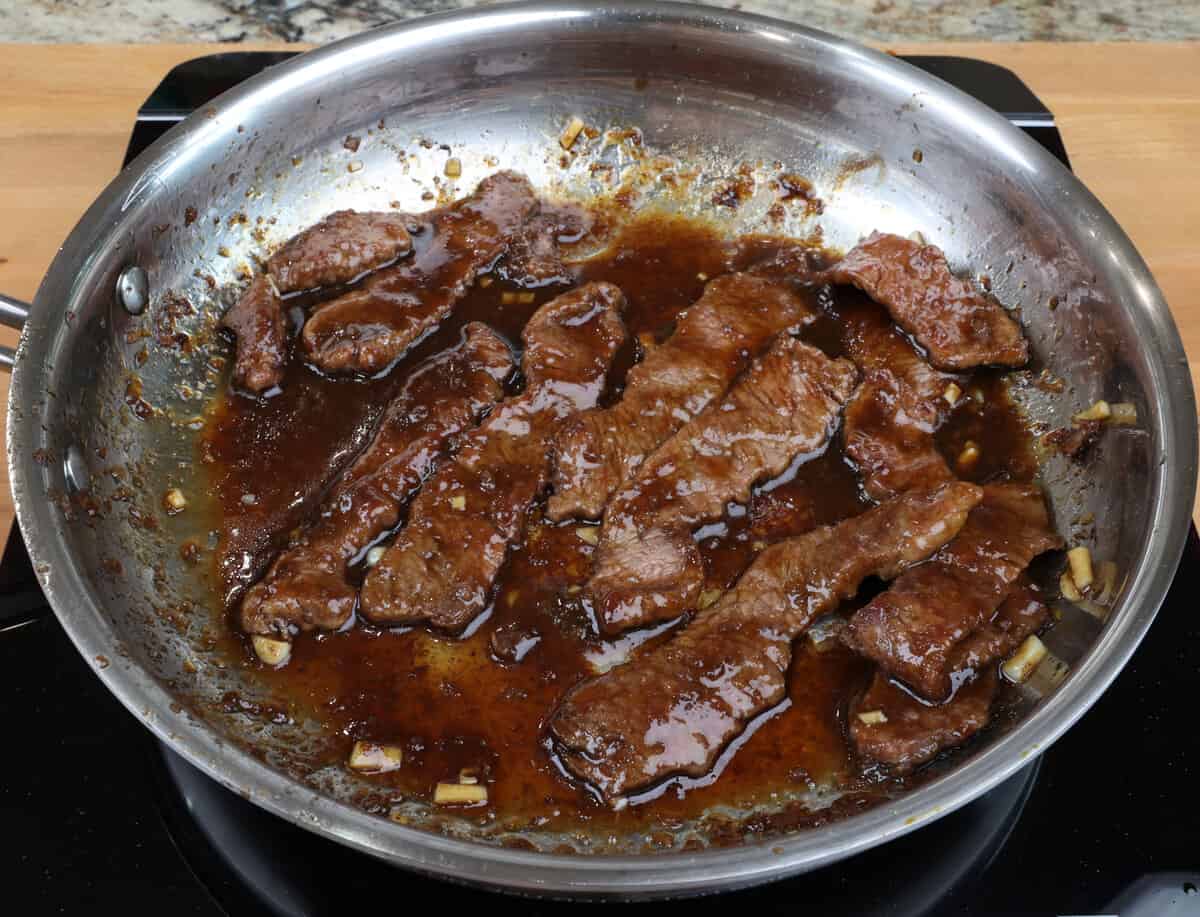 mongolian beef simmering in a skillet on the stove.