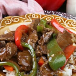 a single serving of pepper steak with red and green bell peppers served on a gold plate
