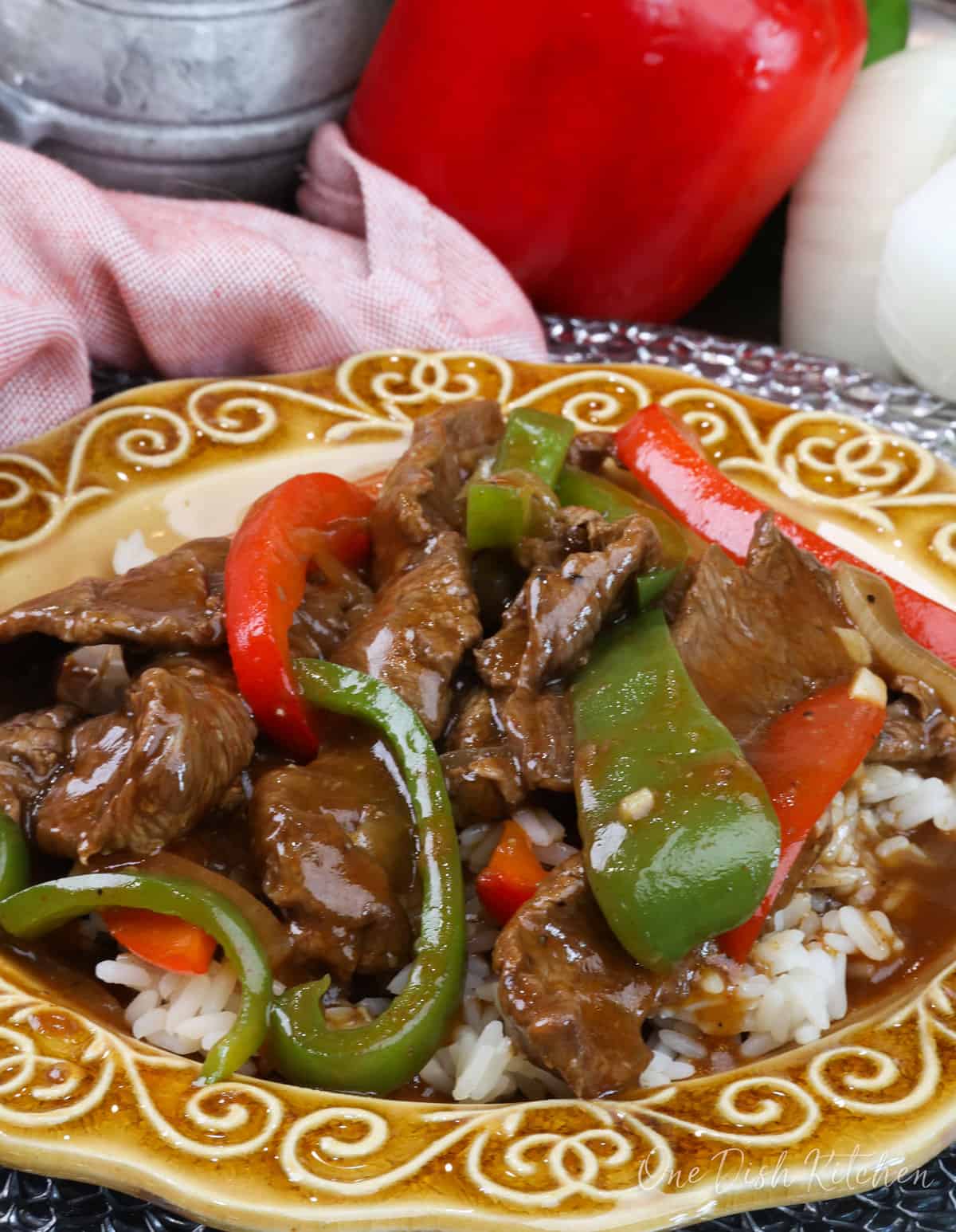 a single serving of pepper steak with red and green bell peppers served on a gold plate.