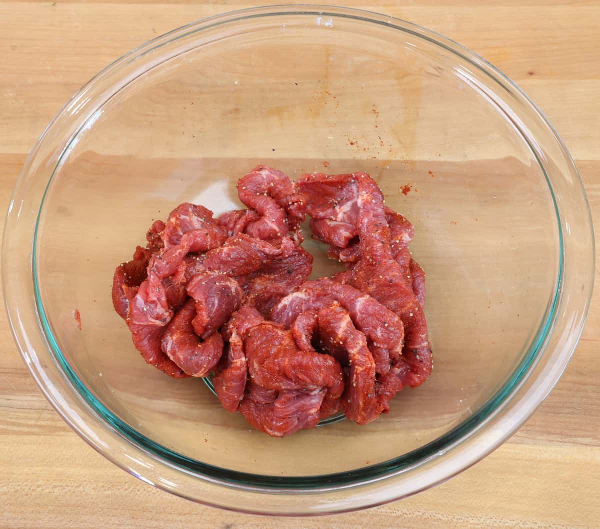 slices of flank steak seasoned with paprika, salt, and pepper in a bowl.