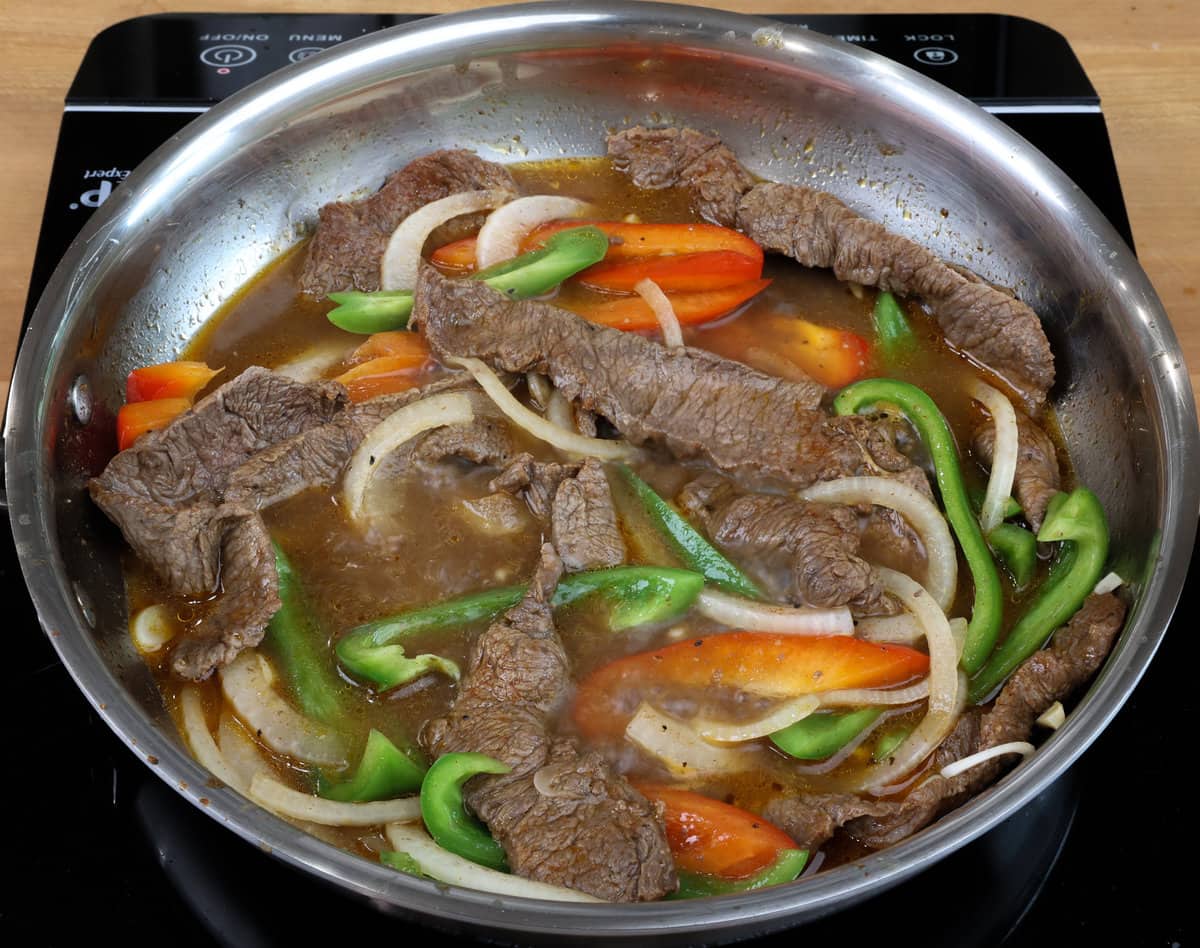 sliced bell peppers and onions simmering in a pan with sliced steak.