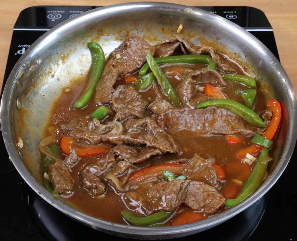 Pepper steak and vegetables cooking in a skillet.