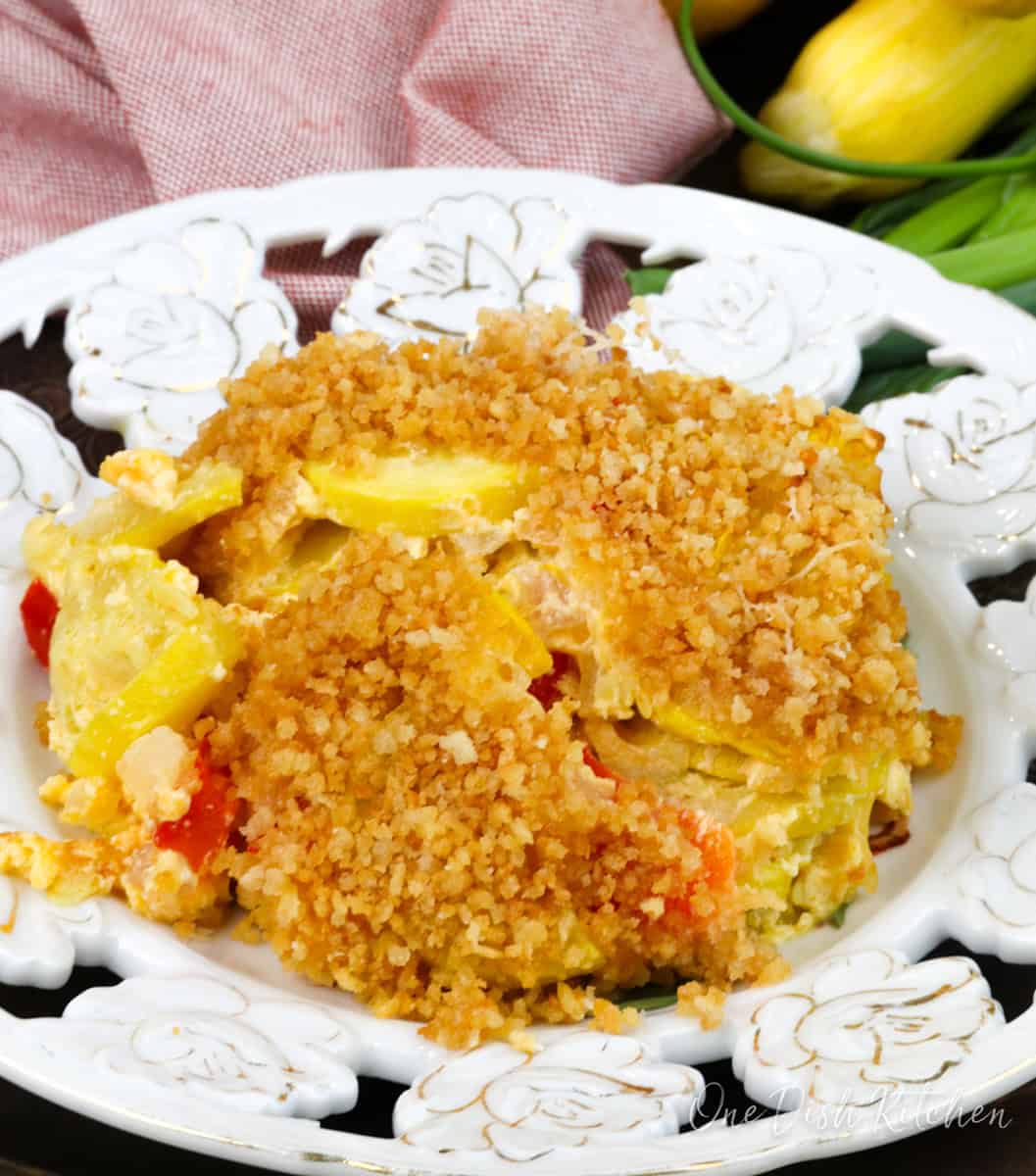 a serving of squash casserole topped with breadcrumbs on a white plate next to an orange napkin.