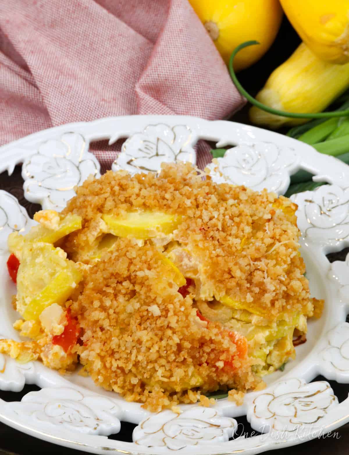 a serving of squash casserole topped with breadcrumbs on a white plate next to an orange napkin.
