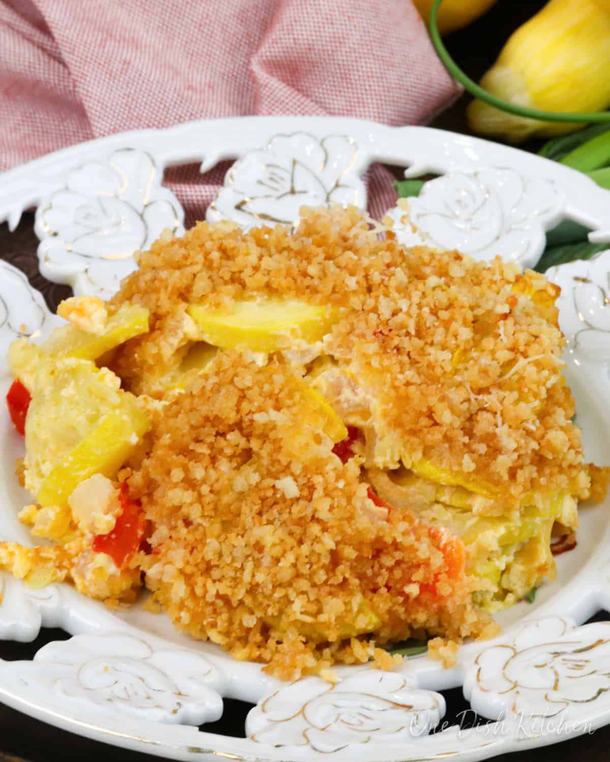 a serving of squash casserole topped with breadcrumbs on a white plate next to an orange napkin.