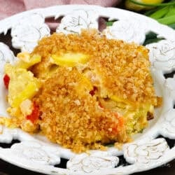 a serving of squash casserole topped with breadcrumbs on a white plate next to an orange napkin.