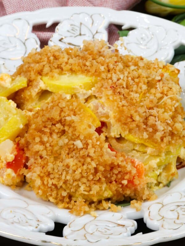 a serving of squash casserole topped with breadcrumbs on a white plate next to an orange napkin.