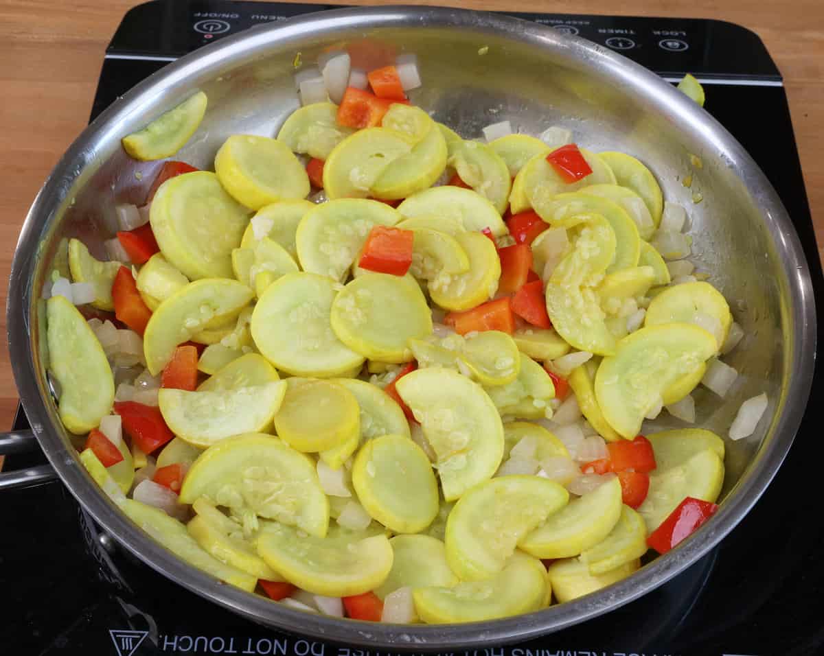 yellow squash, onions, red bell peppers cooking in a skillet.