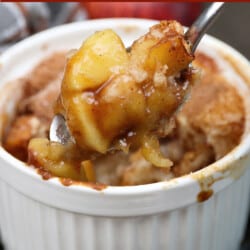 a small apple cobbler with the spoon above the dish filled with apples