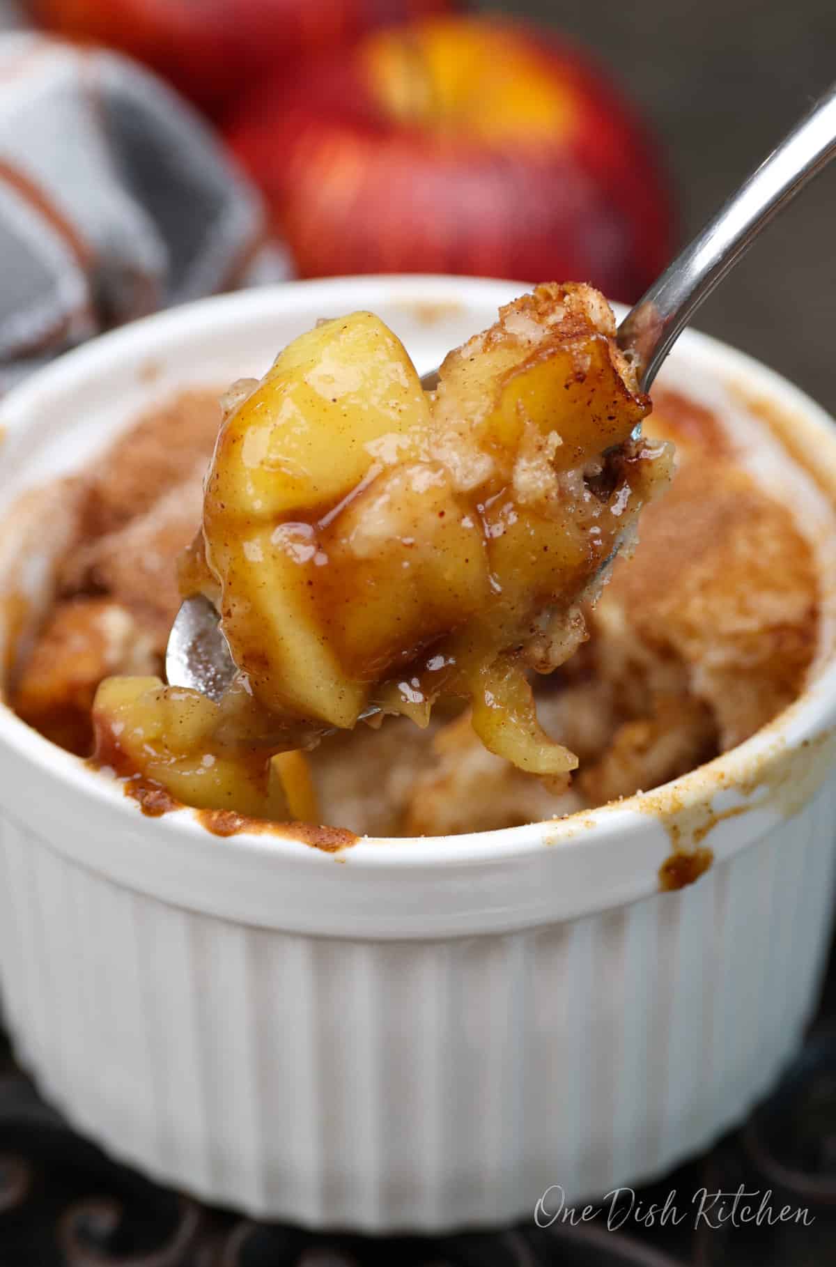 a small apple cobbler with the spoon above the dish filled with apples.