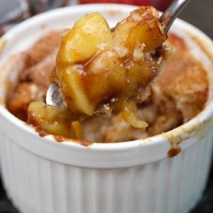a small apple cobbler with the spoon above the dish filled with apples
