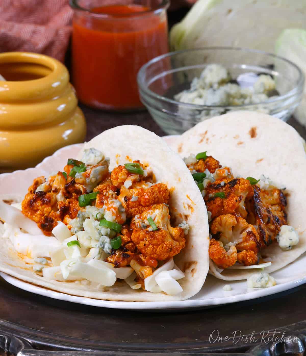 two buffalo cauliflower tacos on a plate topped with buffalo sauce, blue cheese, and shredded cabbage.