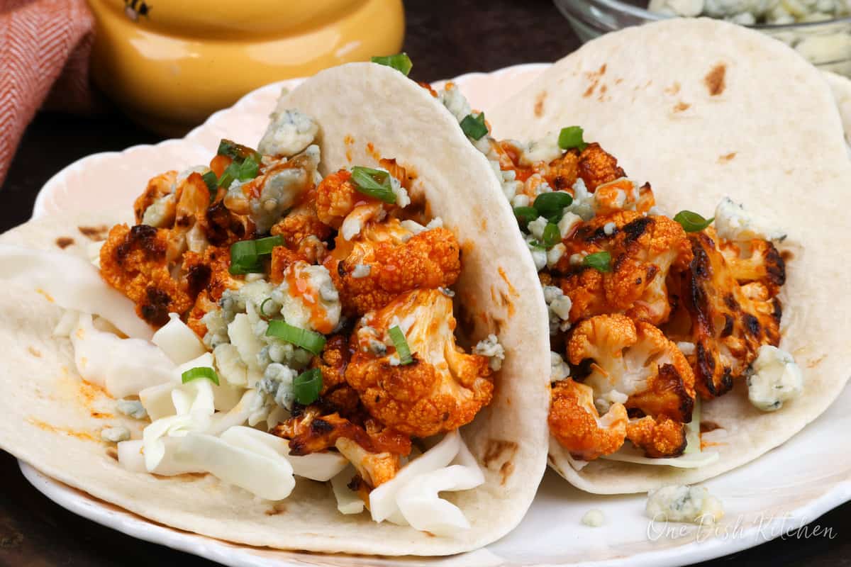 two buffalo cauliflower tacos with shredded cabbage and blue cheese on top.