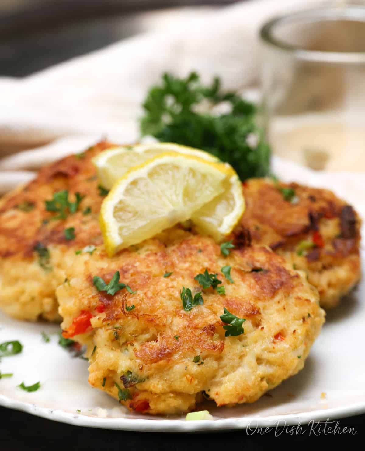 three crab cakes on a white plate topped with lemon slices.