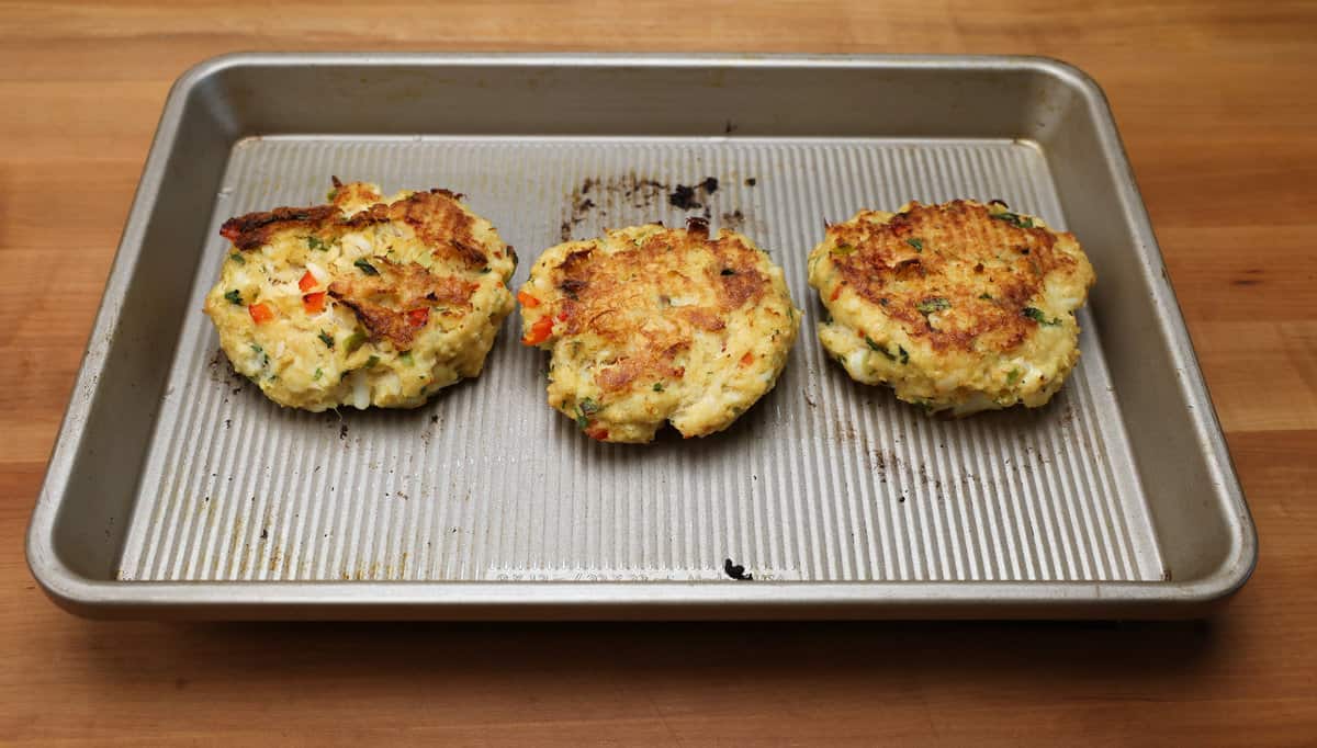 three baked crab cakes on a baking sheet.