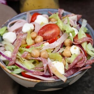 an italian chopped salad in a bowl next to a jar of vinaigrette