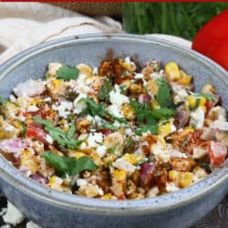 a blue bowl filled with Mexican street corn salad next to a red bell pepper and cilantro