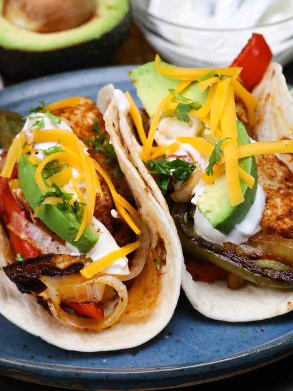 2 chicken fajitas topped with avocado slices, sour cream and cheese on a blue plate.