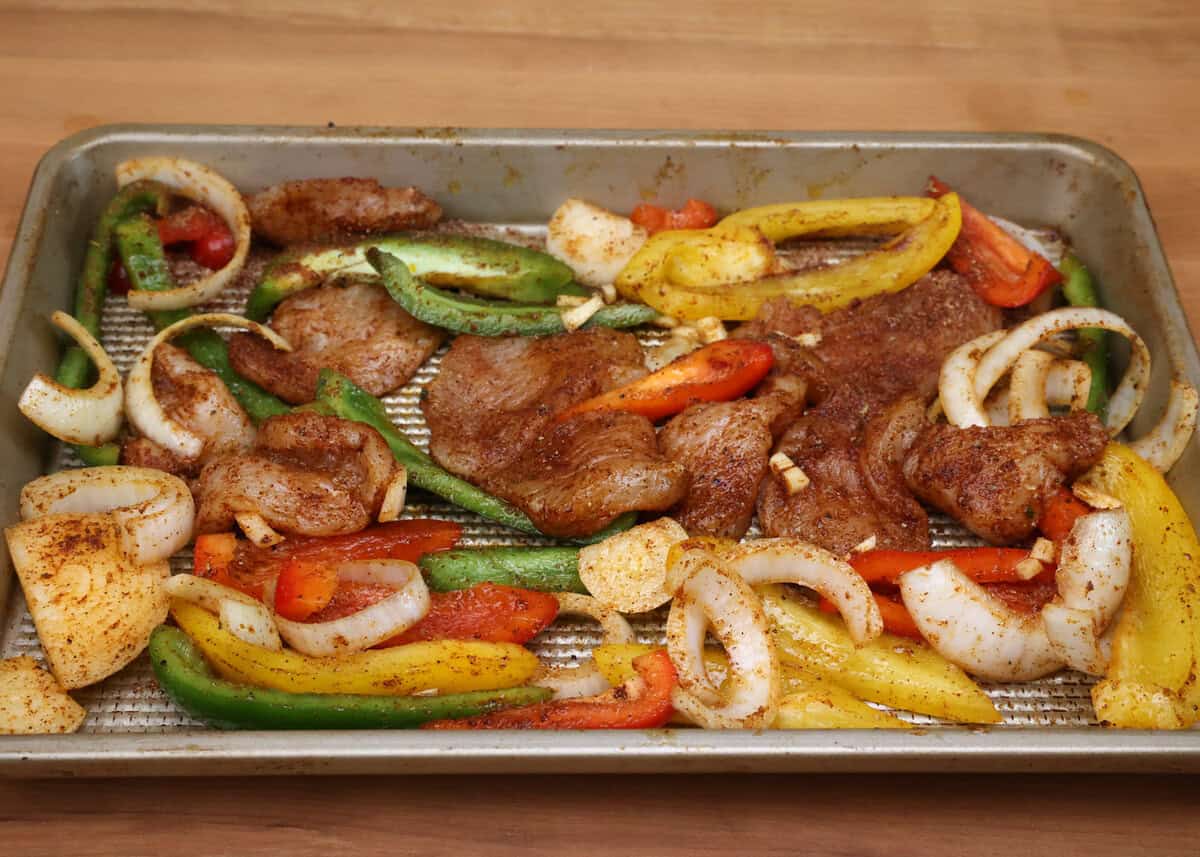 seasoned chicken strips and slices of onions and bell peppers on a sheet pan.