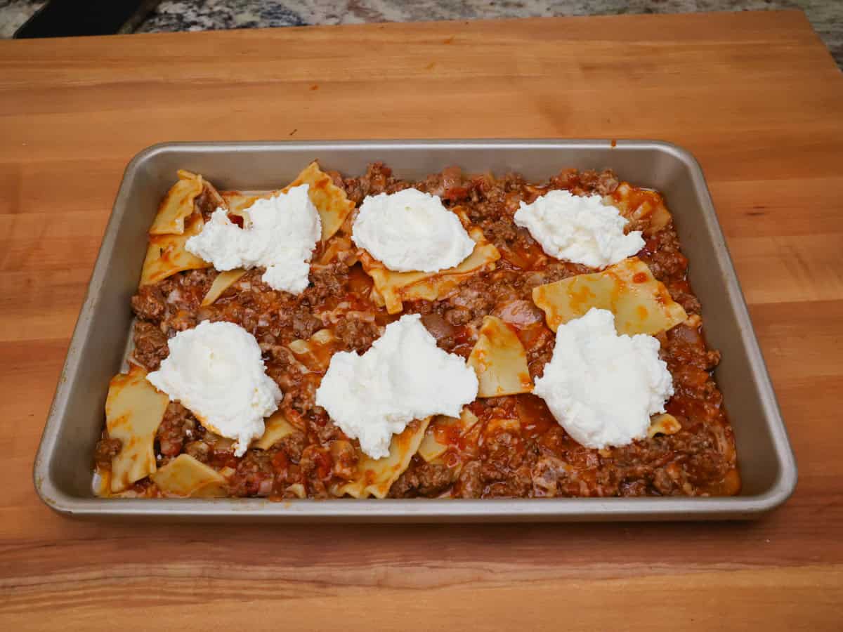 dollops of ricotto on top of lasagna noodles and beef.