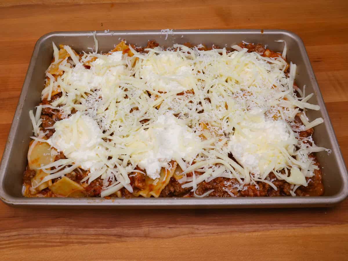 unbaked lasagna topped with cheese on a sheet pan.
