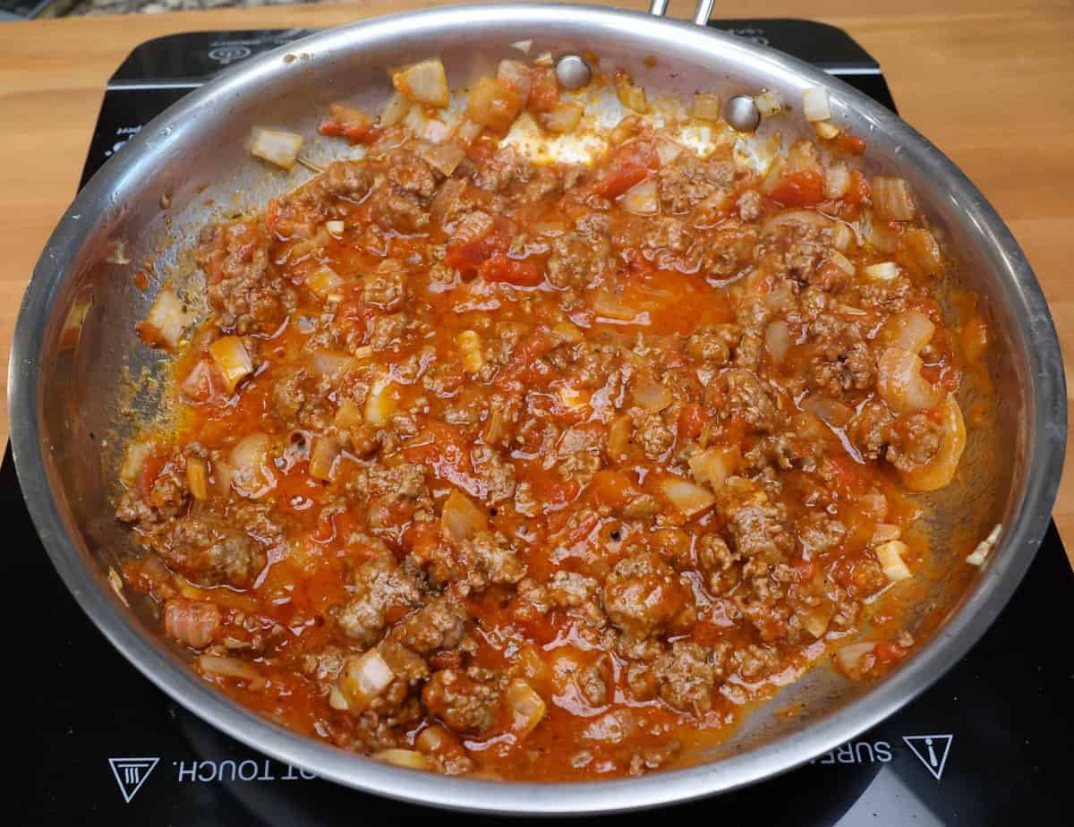 tomato sauce, ground beef, onions and garlic simmering in a skillet.