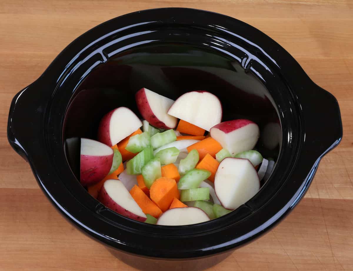 celery, carrots, onions, and potatoes in a slow cooker.