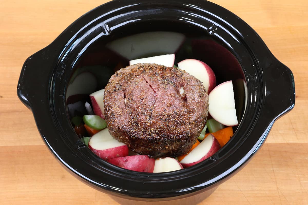 beef on top of vegetables in a slow cooker.