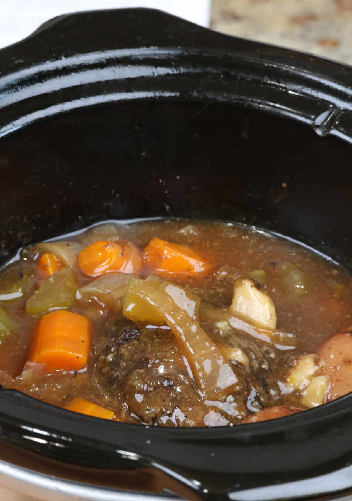 a pot roast in a slow cooker surrounded by vegetables.