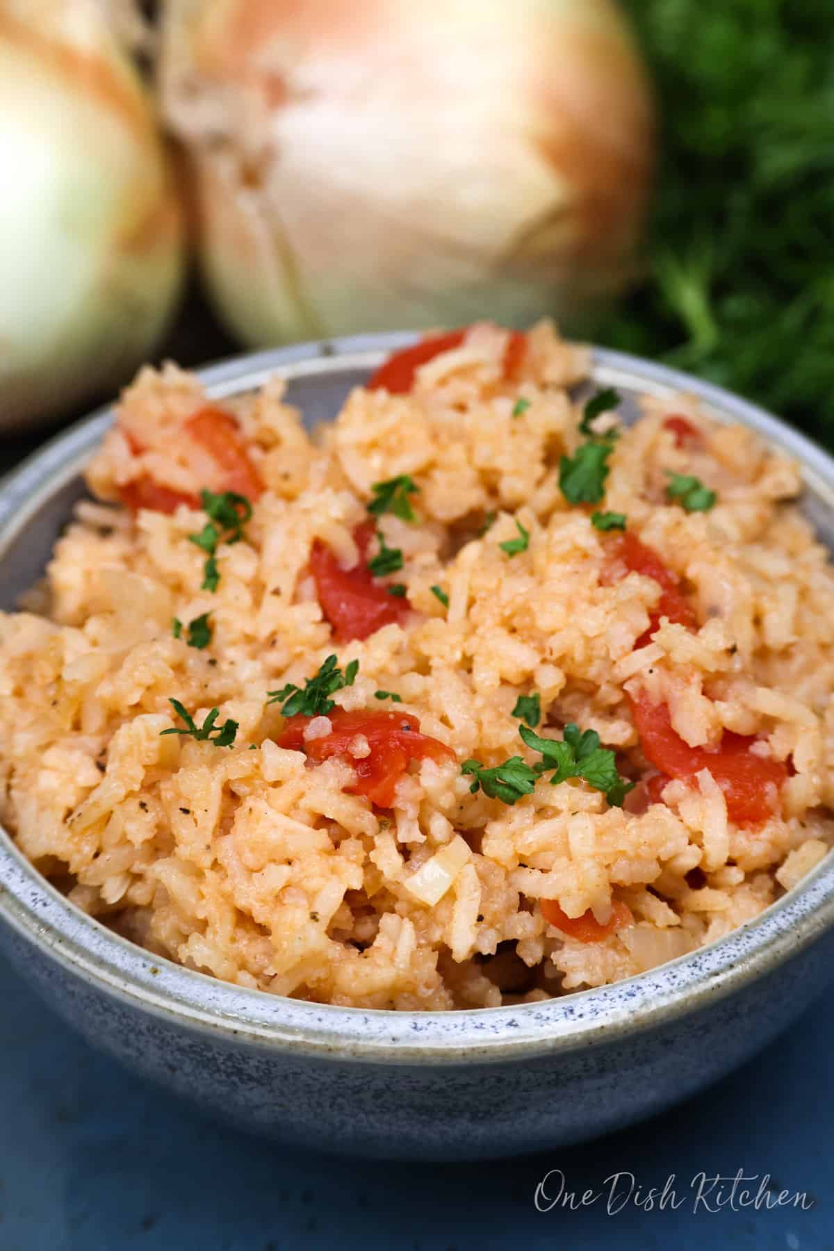 a blue bowl filled with spanish rice next to two onions.