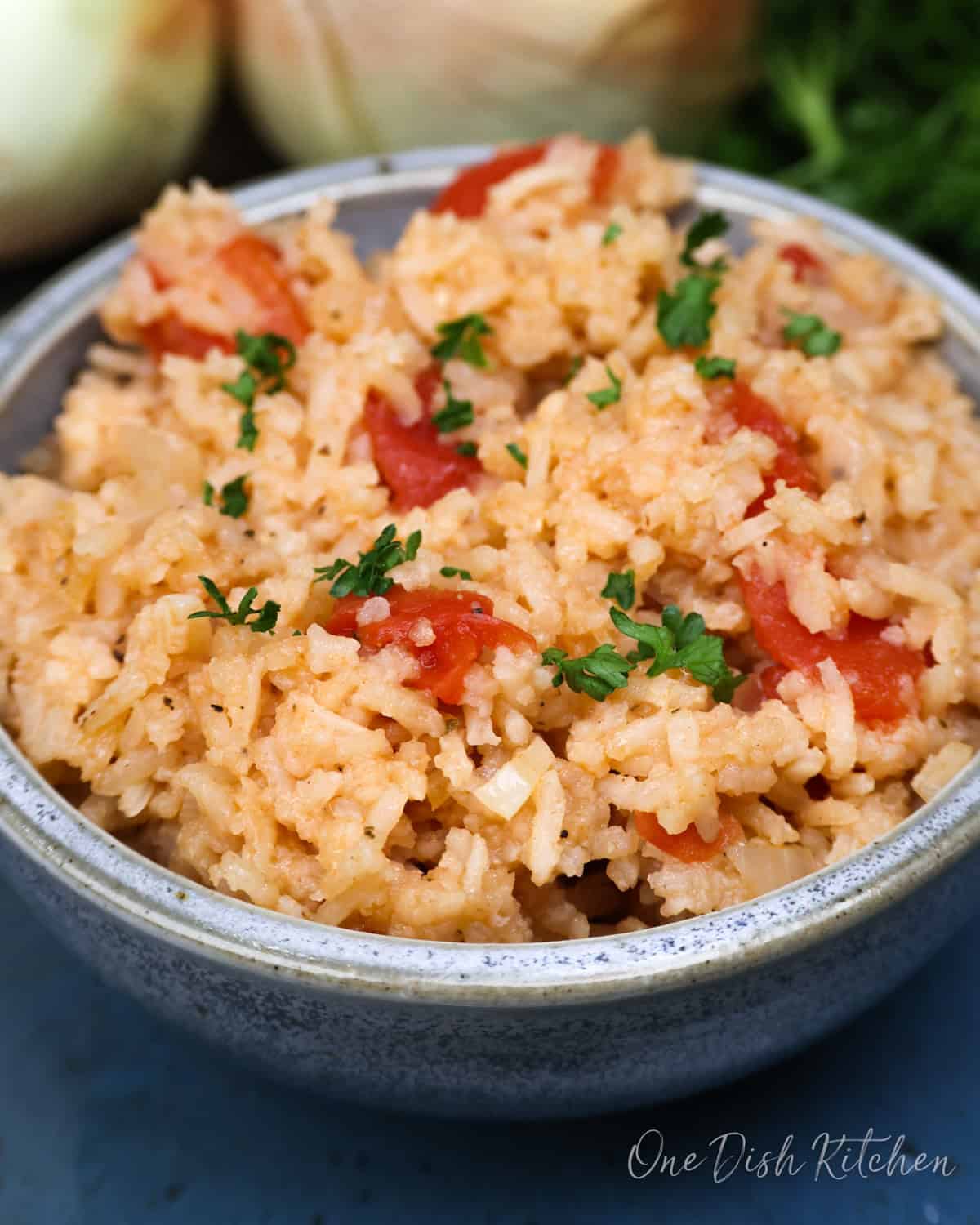 a blue bowl filled with spanish rice next to two onions.