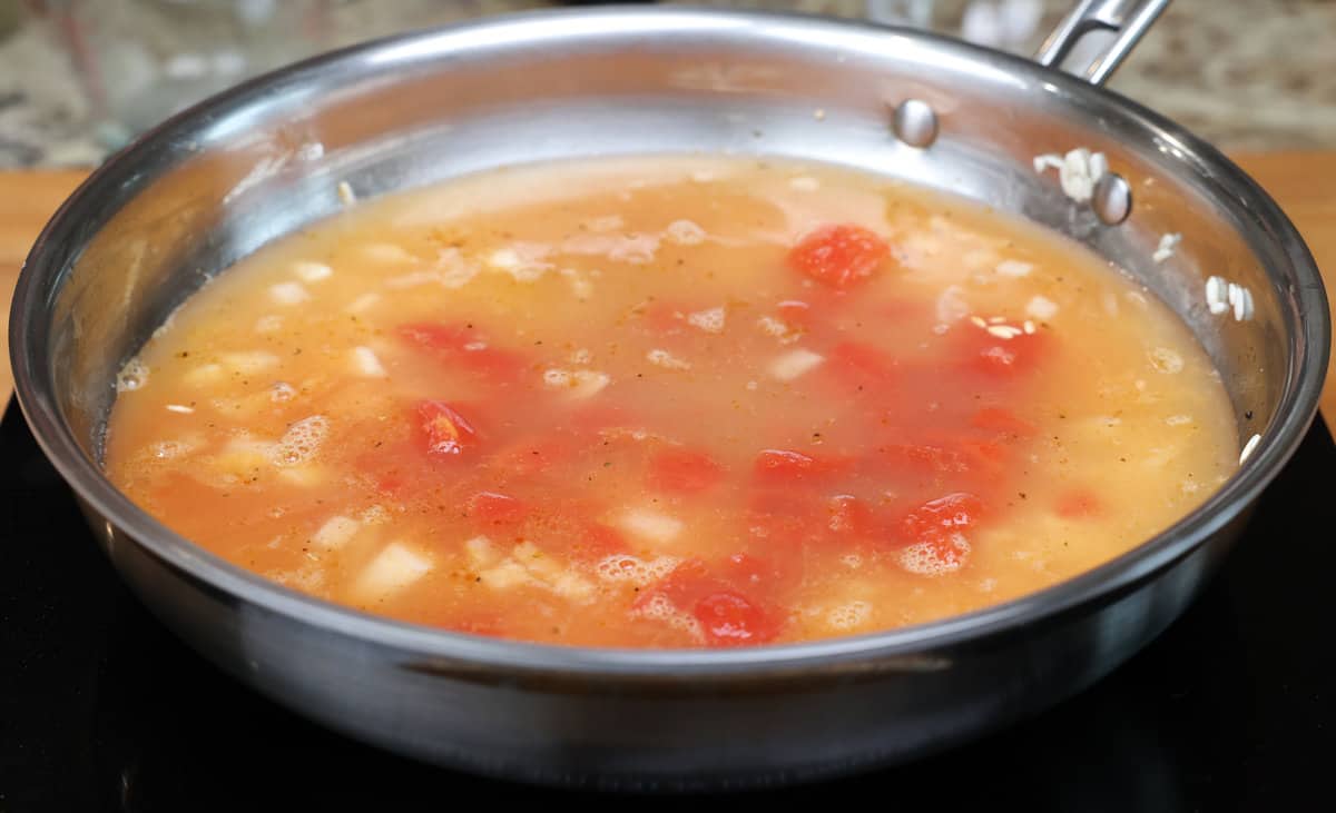 rice, broth, and diced tomatoes simmering in a skillet.