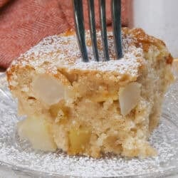 a slice of apple cake topped with powdered sugar on a white plate next to an orange napkin.