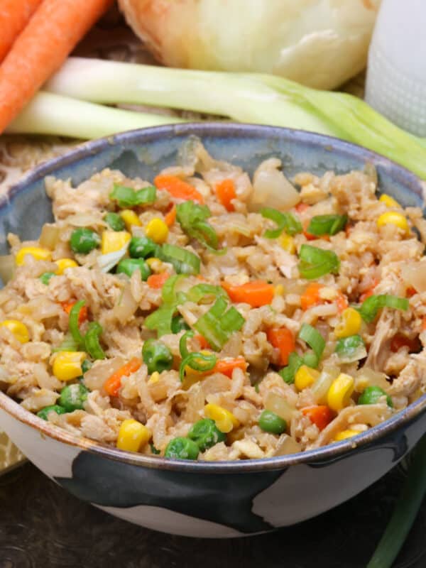 a bowl of chicken fried rice next to carrots and celery and a brown napkin.