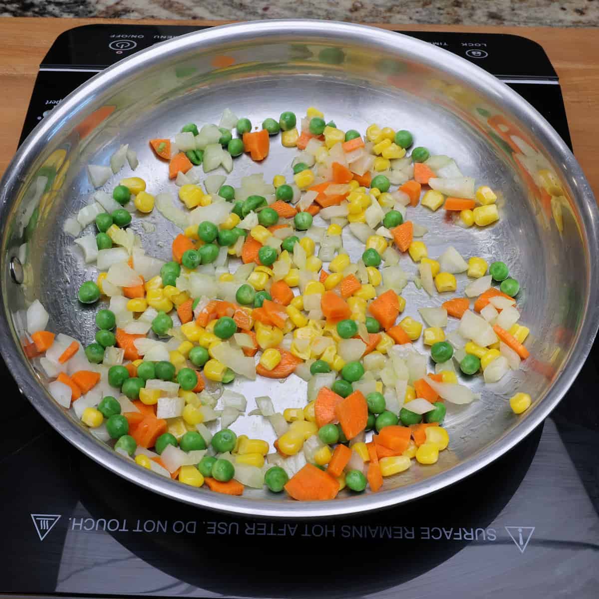 carrots, peas, corn, and onions cooking in a skillet.