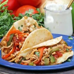 two chicken tacos on a plate next to a jar of sour cream.