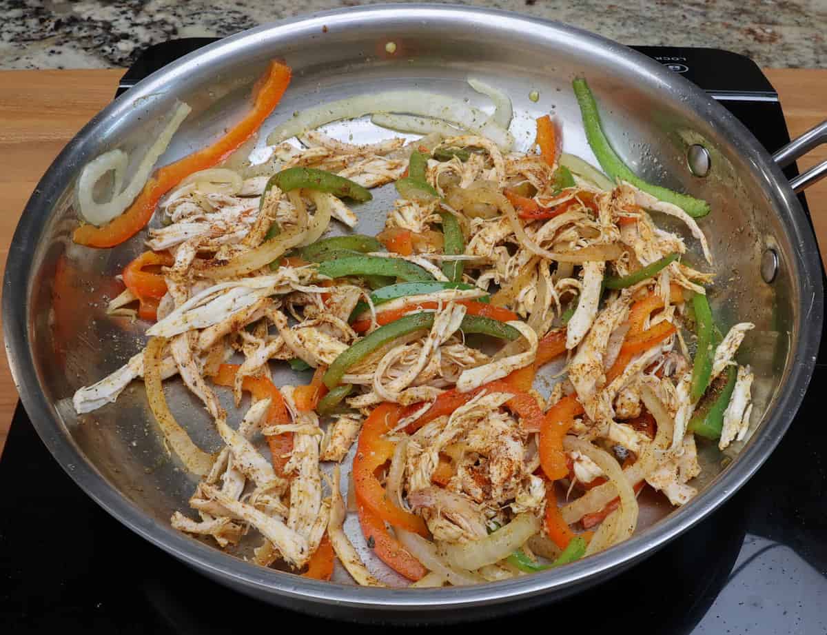shredded chicken, sliced onions and sliced bell peppers in a skillet.