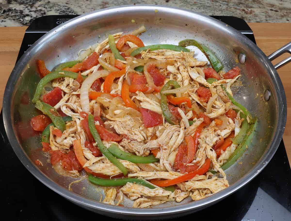 diced tomatoes, chicken, and vegetables cooking in a skillet.