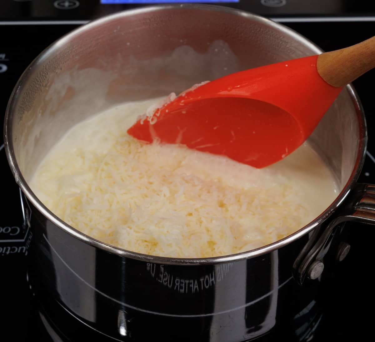shredded parmesan cheese in a pot of heavy cream simmering on the stove.