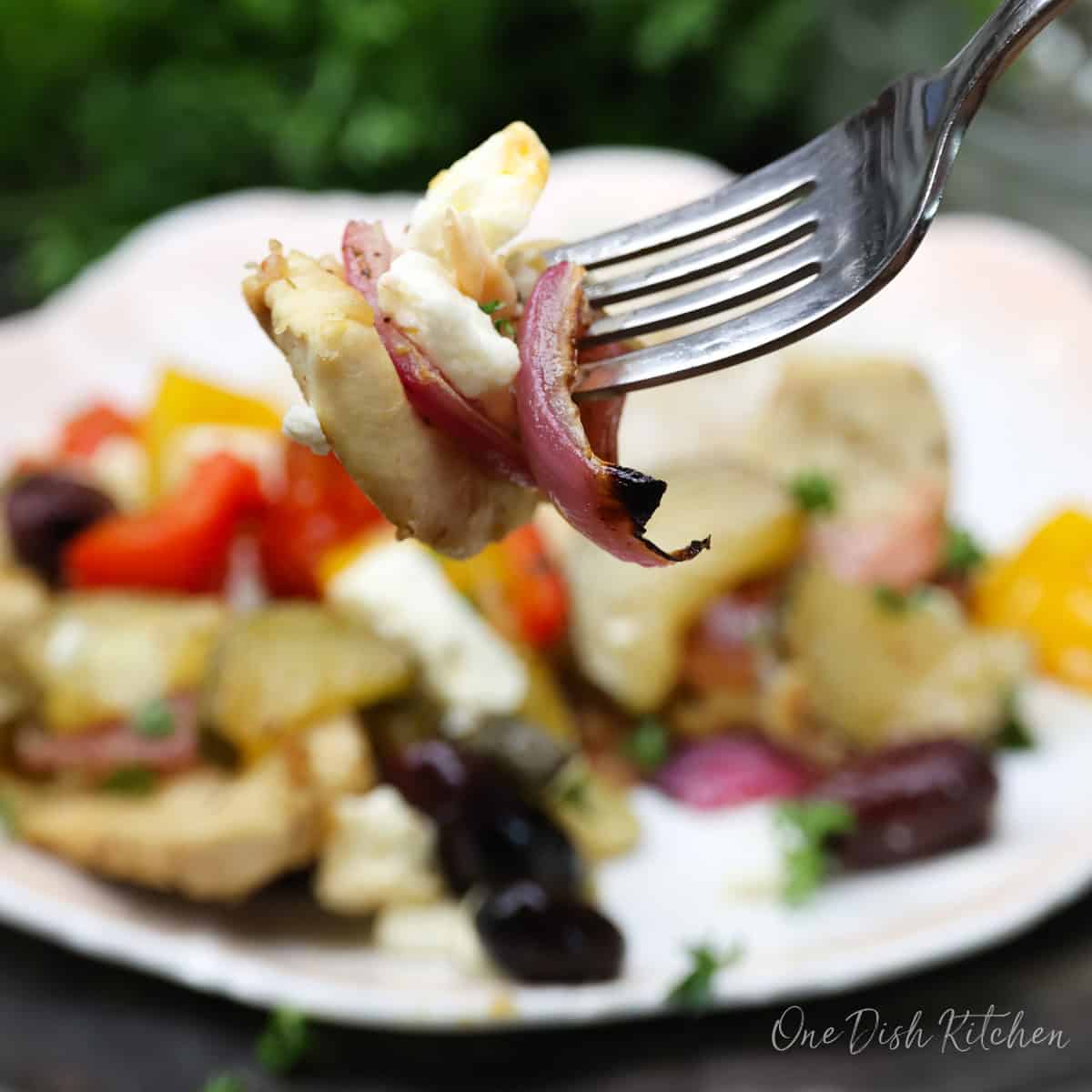 a fork filled with chicken and onions above a plate of vegetables.