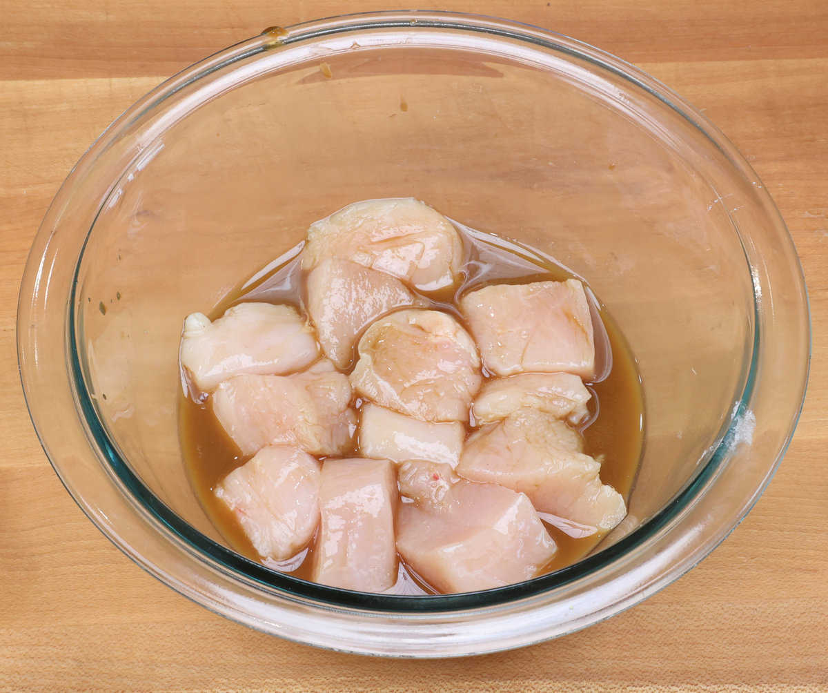 chicken pieces marinating in kung pao chicken sauce in a small bowl.
