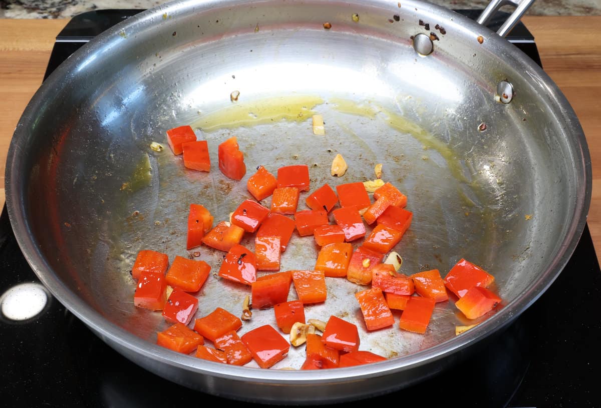 chopped red bell pepper and garlic cooking in a skillet.