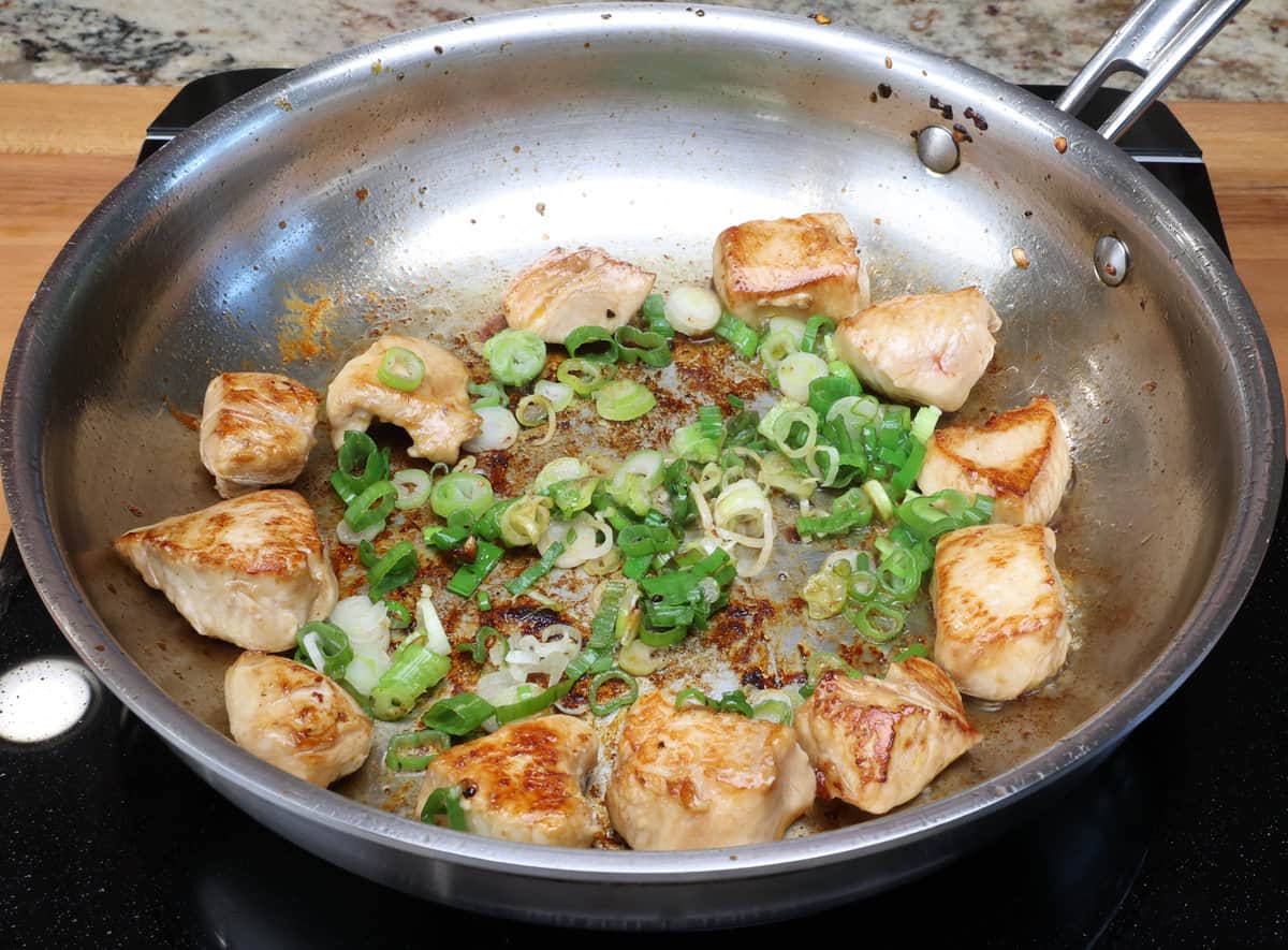 chicken and green onions cooking together in a small skillet.