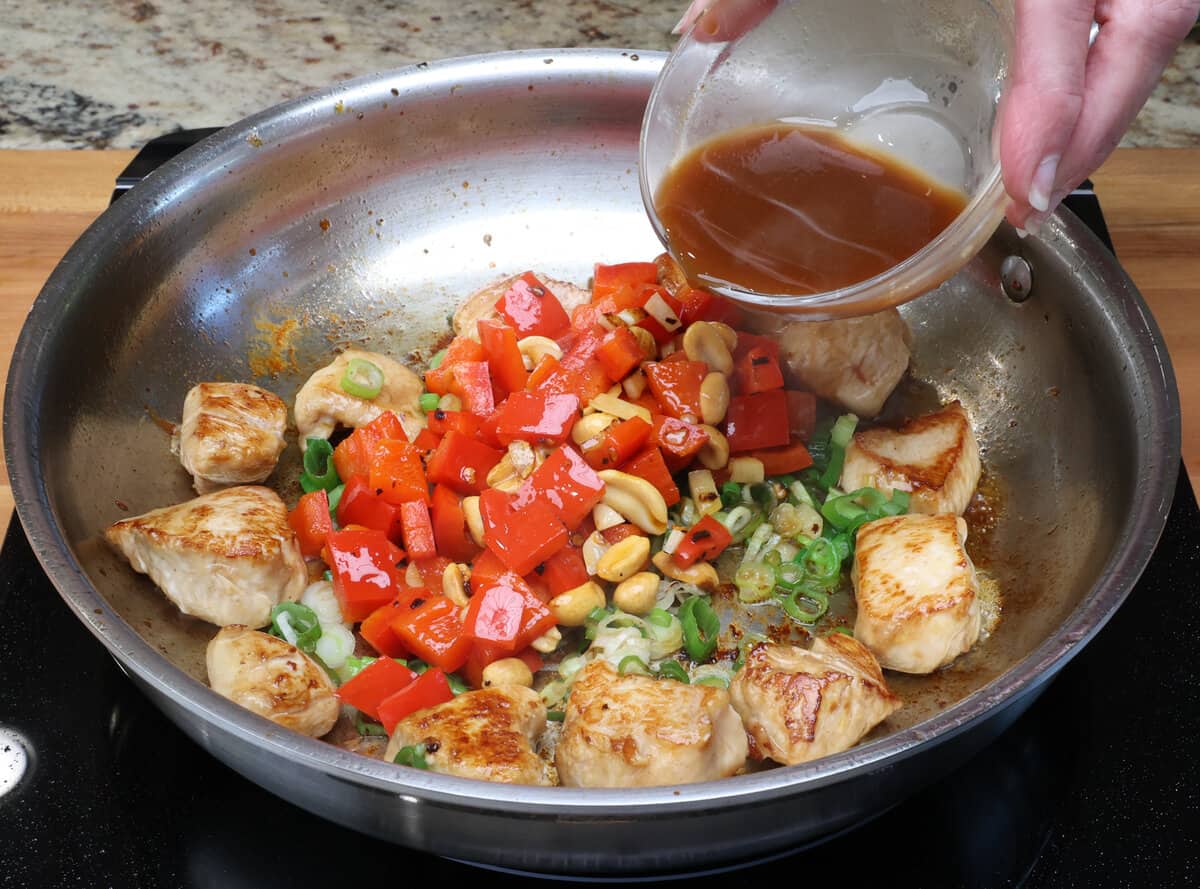 kung pao sauce poured into a skillet with chicken, peanuts, and vegetables.